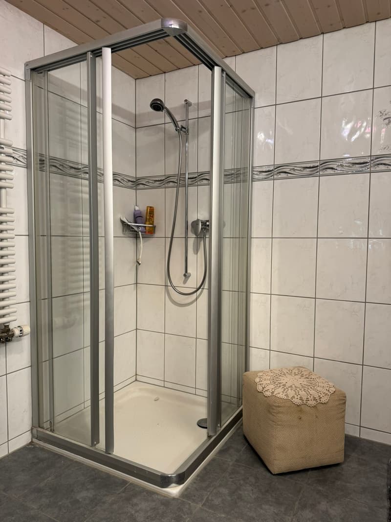 shower stall, white tiles, silver shower head, small stool, toiletries
