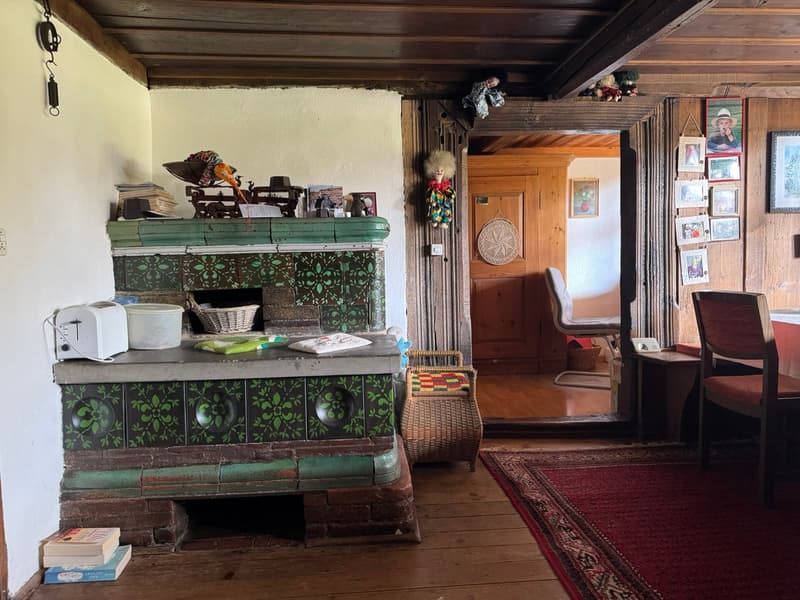 Fireplace with green tiles, toaster, books, basket, wicker basket, pictures on wall, wooden floor, wooden door, chair, table, rug