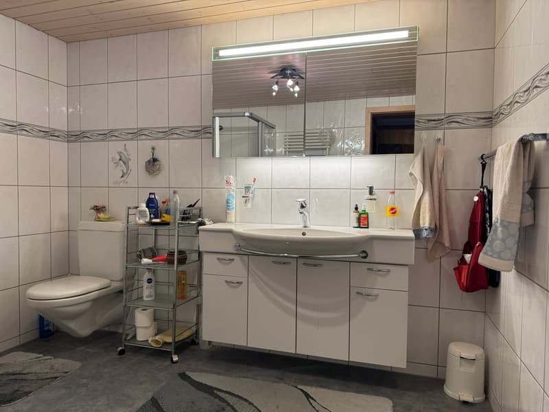 white tiled walls, white sink, mirror, toilet, shelves, towels, toiletries