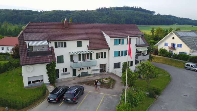 2 story house, brown roof, white walls, 2 balconies, 2 cars parked in front