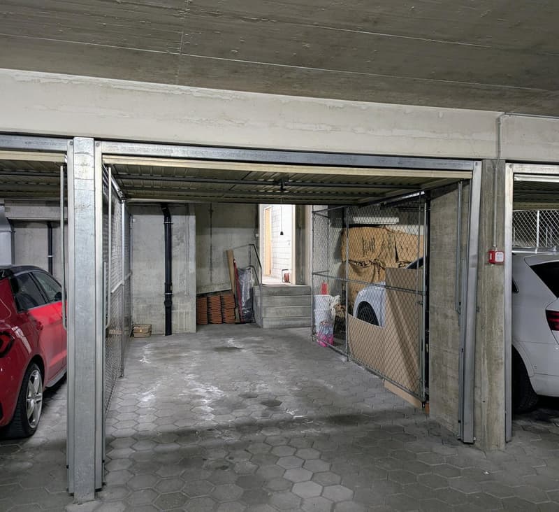 underground parking lot, two cars parked, storage boxes, metal fences, stairs