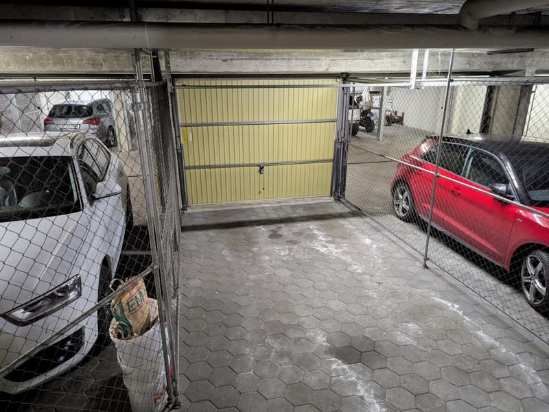 underground parking lot with cars parked, yellow gate, metal fence, trash cans
