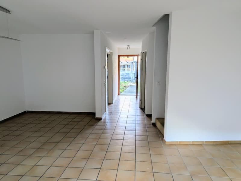 Empty hallway with tiled floor, white walls, open door leading to outside