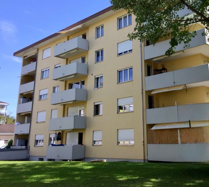 5 story apartment building, yellow exterior, multiple balconies, green lawn in front