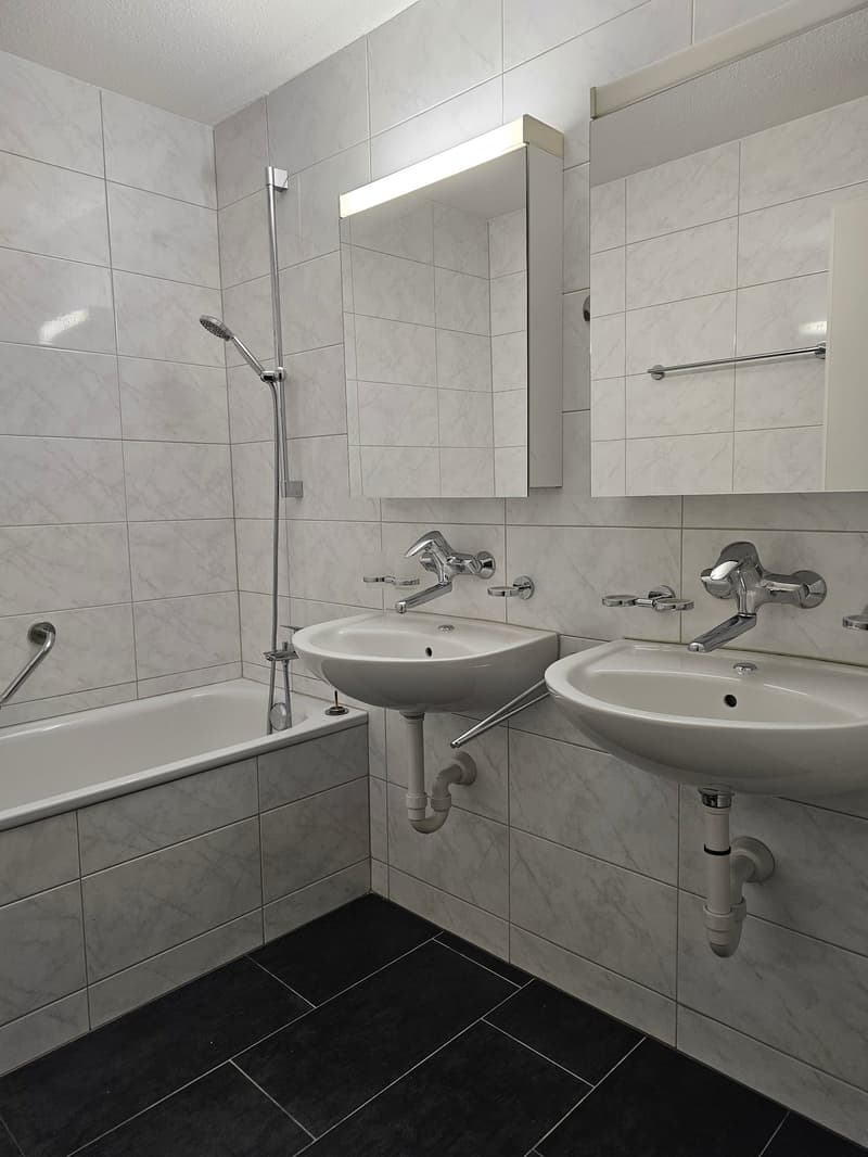 Bathroom with white tiles, bathtub, two sinks, shower head, and mirrors