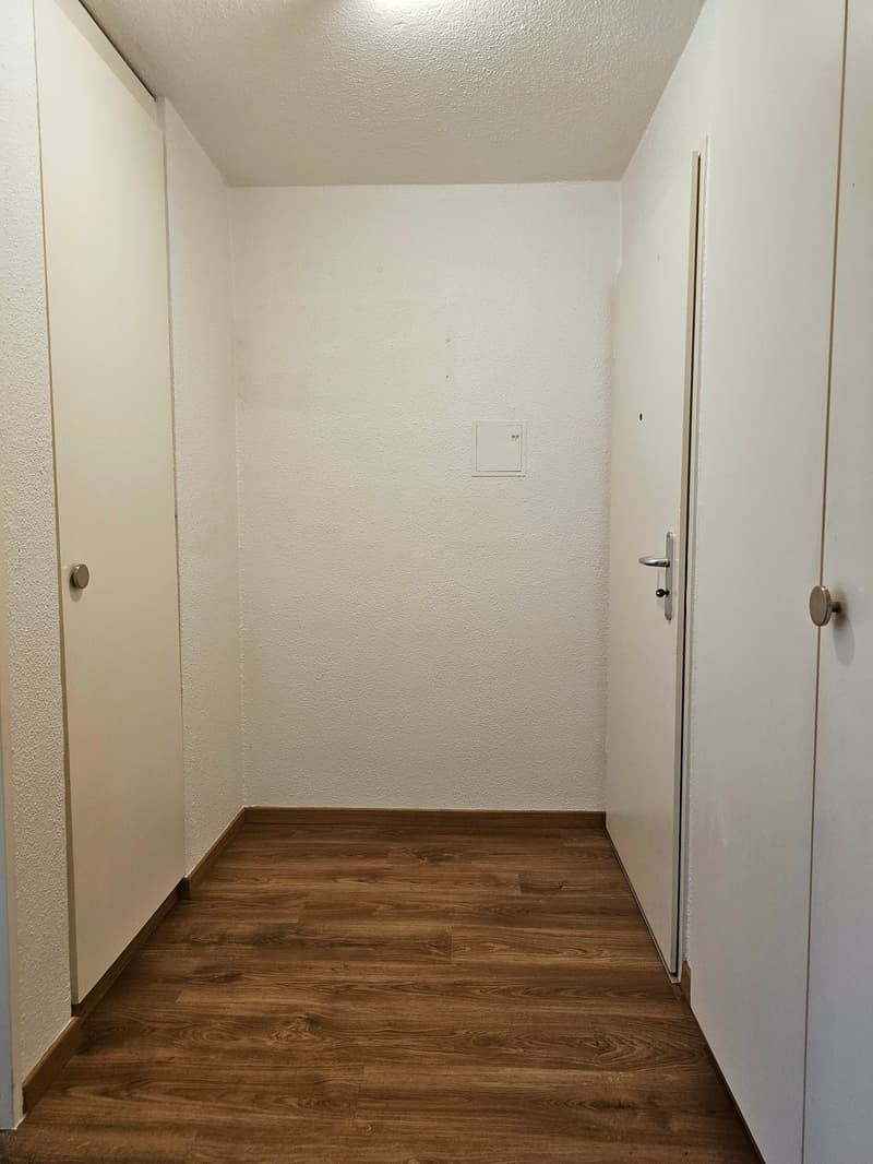 Empty room with wooden floor, white walls, two doors, and a power outlet on the wall.