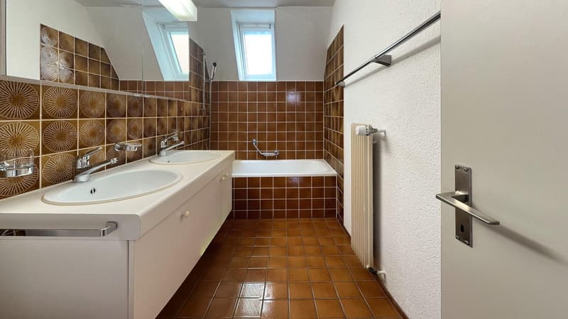 Bathroom with two sinks, bathtub, radiator, brown tiles, two windows