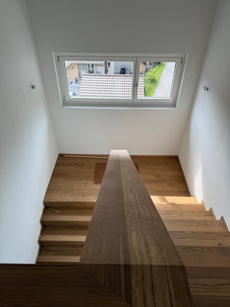 Wooden staircase with a large window overlooking the rooftops and greenery outside.