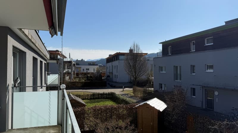 Residential apartment building with terrace, nearby garden, multiple buildings, distant mountains