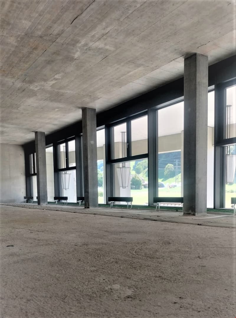 Concrete pillars, large windows, empty interior, hanging lamps, exposed beams, concrete floor