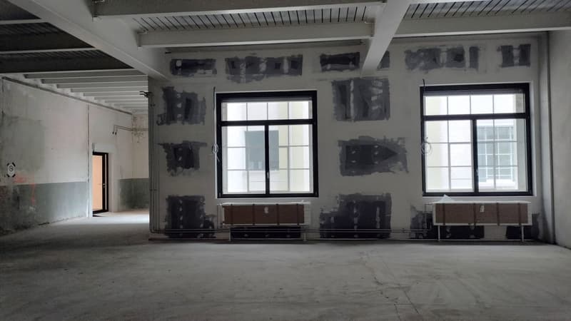 Open space with exposed ceiling, concrete floor, unfinished walls, two large windows, industrial look, and an open door on the left.