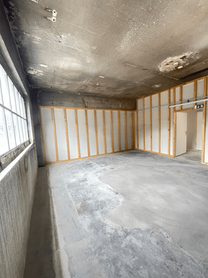 Unfinished room with exposed wooden framing, concrete floor, and damaged ceiling. The room appears to be in a state of renovation or disrepair.