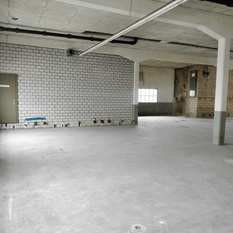 Large open room with white brick walls, concrete floor, and exposed ceiling beams. The space appears to be an unfinished interior, possibly a commercial or industrial building undergoing renovation or construction.