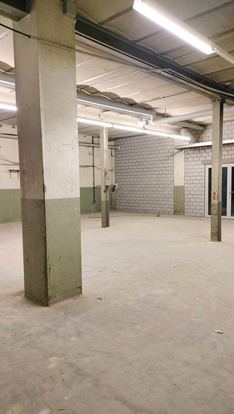 Industrial space with concrete flooring, exposed brick wall, white ceiling with recessed lighting, concrete support columns.