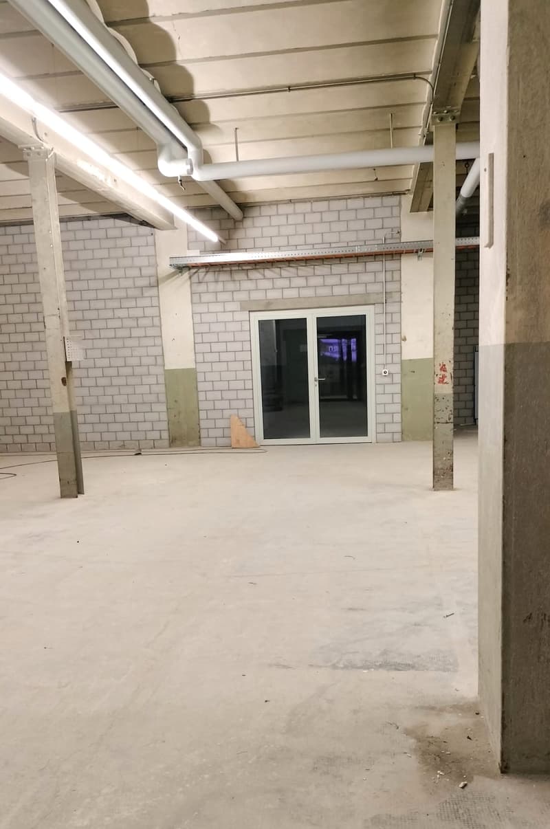 Large open space, white brick walls, exposed ceiling with pipes, metal support beams, sliding glass doors