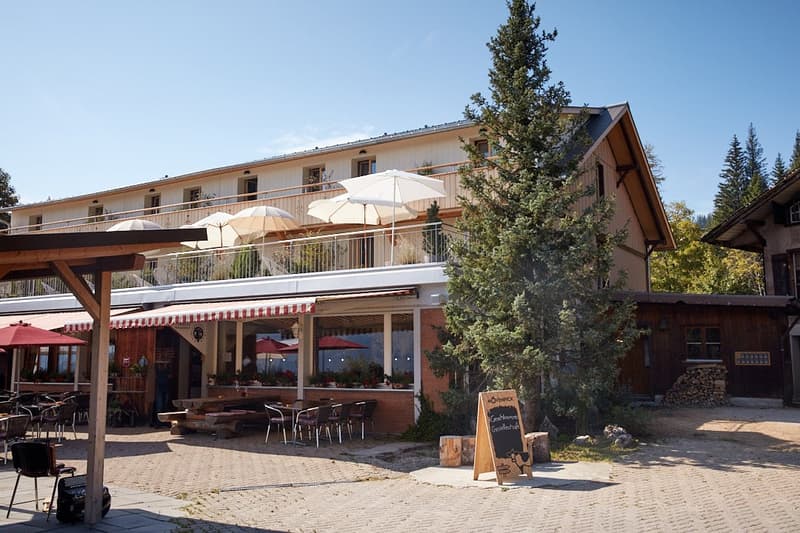 Hotel exterior, red and white striped awning, balconies, outdoor seating with umbrellas, patio, tables and chairs, potted plants, wooden pillars