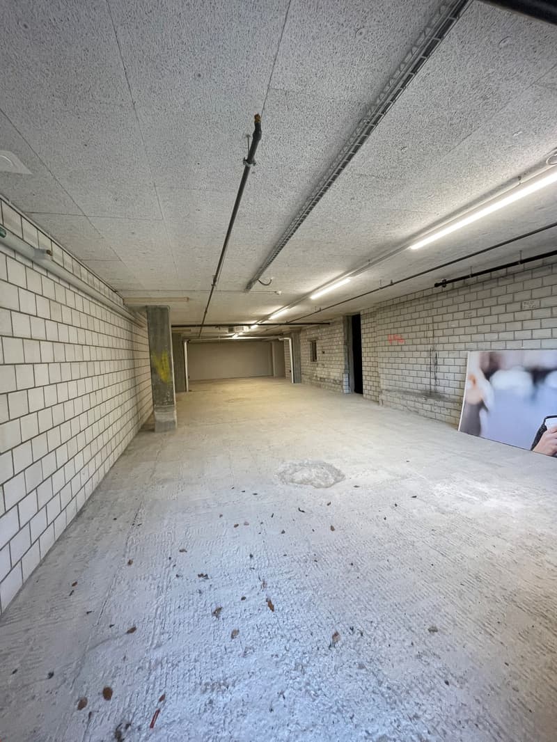 Empty parking space with white tiles, concrete ceiling, metal beams, and concrete support columns.