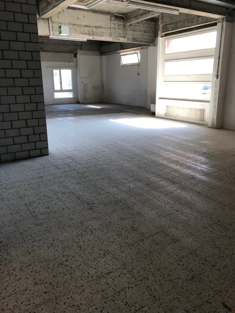 Large open space with concrete floor, exposed brick walls, and windows providing natural light.