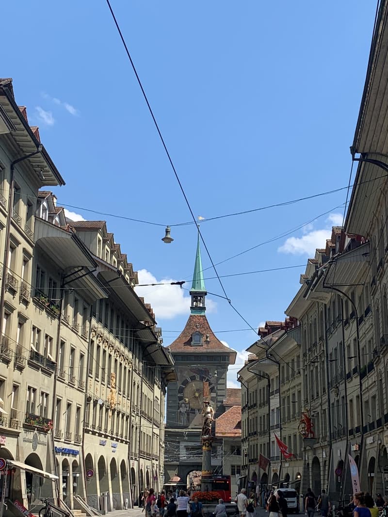 people walking on street with many old buildings, many balconies, large clock tower