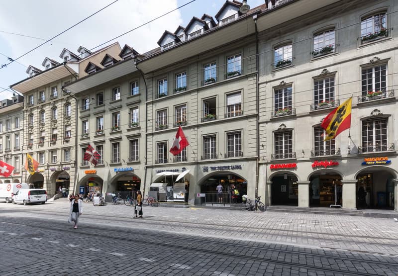 5-story urban building, with multiple shops at the ground floor, various flags displayed