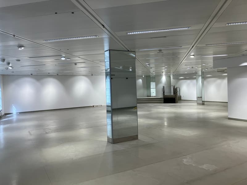 empty commercial space, white walls, ceiling with linear lights, pillar, stairs, floor with reflective tiles