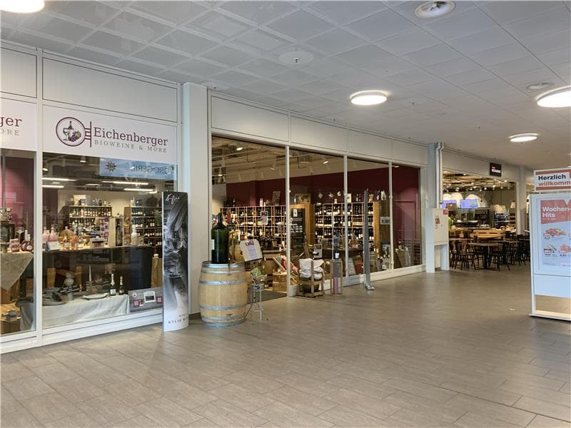 Entrance of a shop with wooden barrels, shelves filled with bottles, and a dining area with tables and chairs.