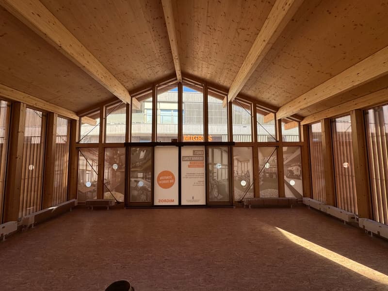 Large open space with wooden beams and ceiling, arched windows, and wooden floors. The space appears to be a gallery or exhibition area with framed artwork or displays on the walls.