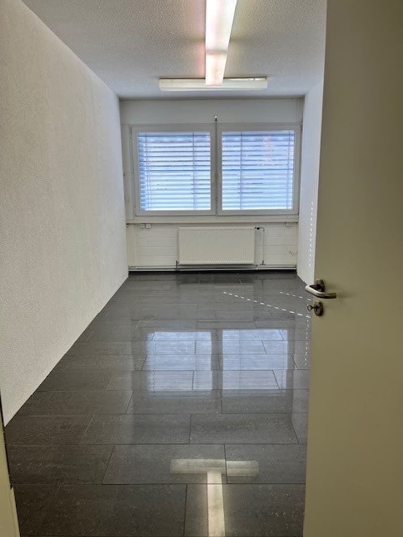 The image shows a room with white walls, a large window with blinds, and a tiled floor. The room appears to be empty, with no furniture or other items visible.