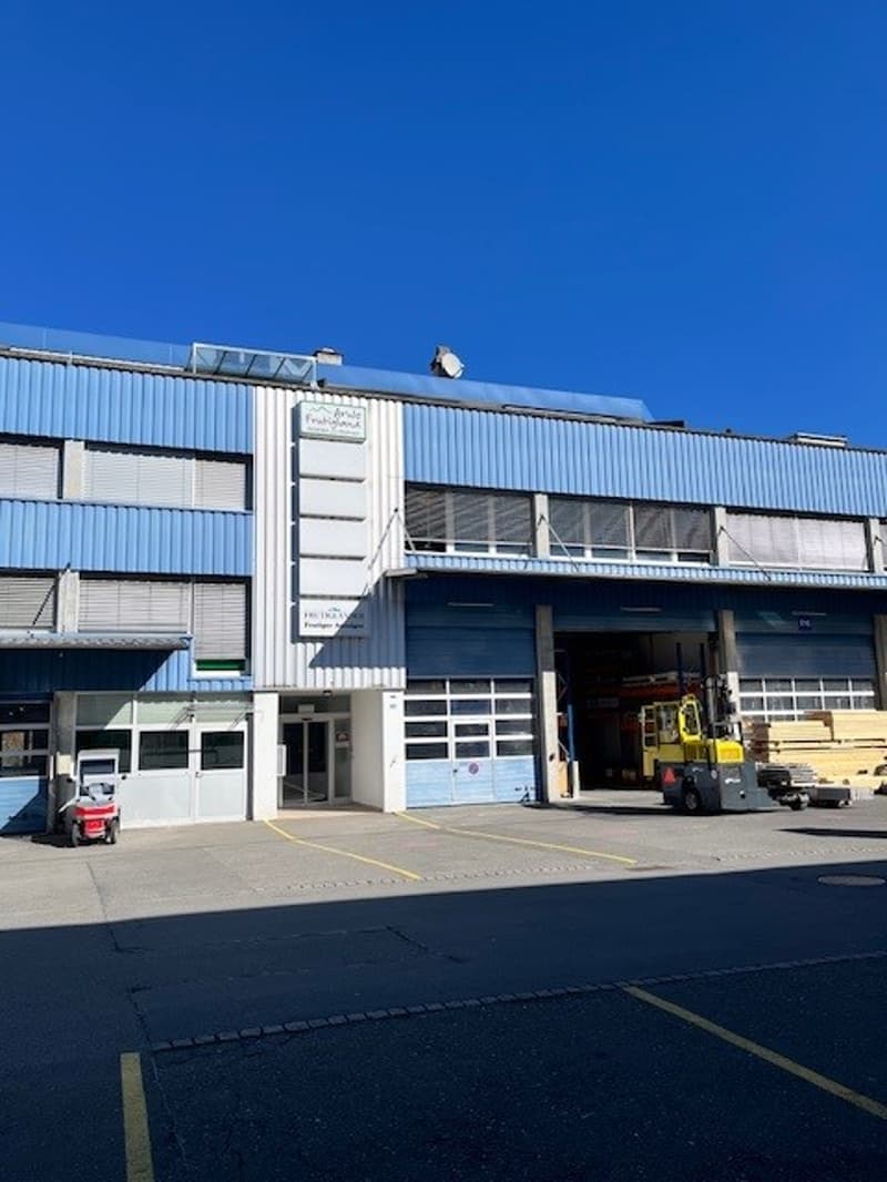 Industrial building, blue exterior, large windows, open garage, forklift, parking lot