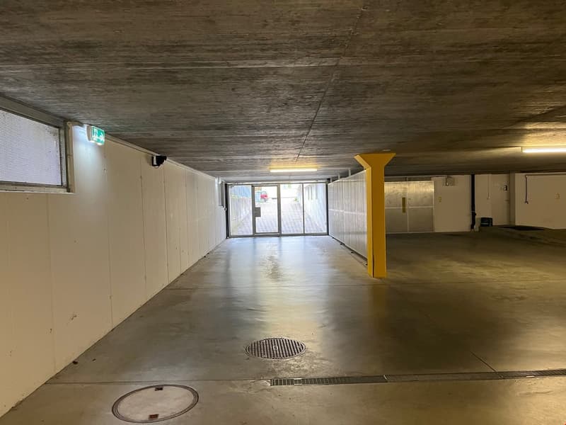 Empty parking area with concrete floor, white walls, yellow pillars, and a glass door.