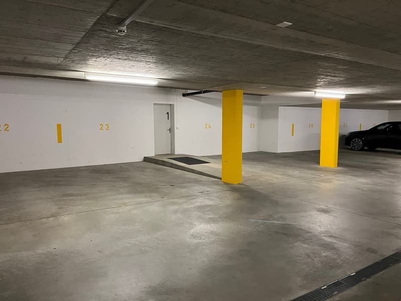 underground parking lot, white walls, yellow pillars, numbered parking spots, a black car parked in spot 27