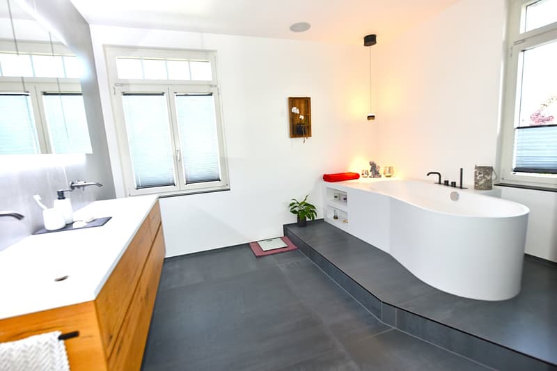 Bathroom with white bathtub, wooden vanity, gray tiled floor, white walls, and a small potted plant