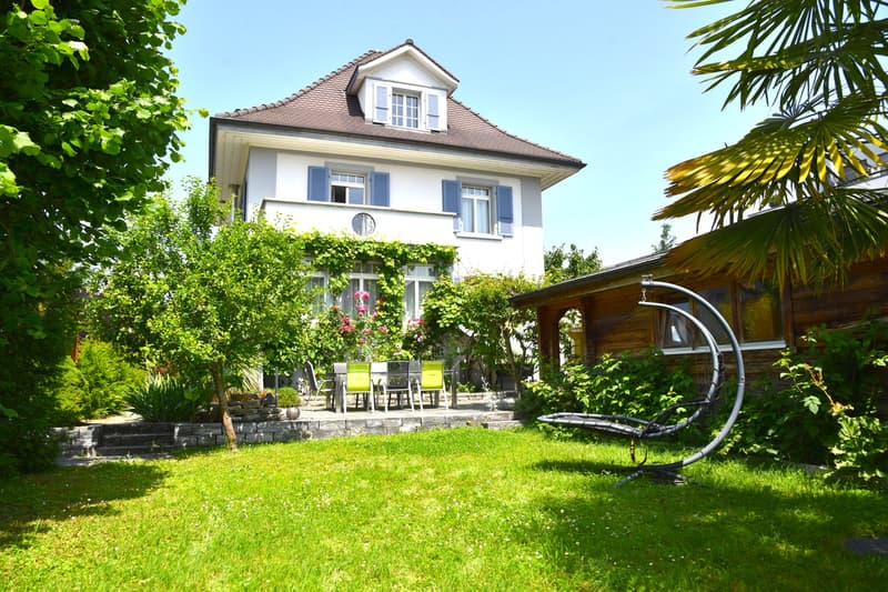 2 story house, white exterior, blue shutters, stone patio, garden, table and chairs, seating swing