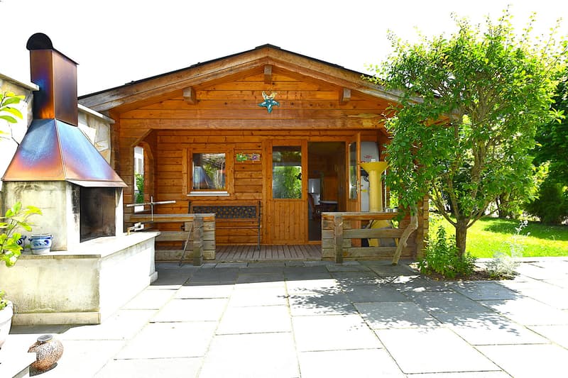 wooden house, brick chimney, stone porch, bench, metal table, trees and plants