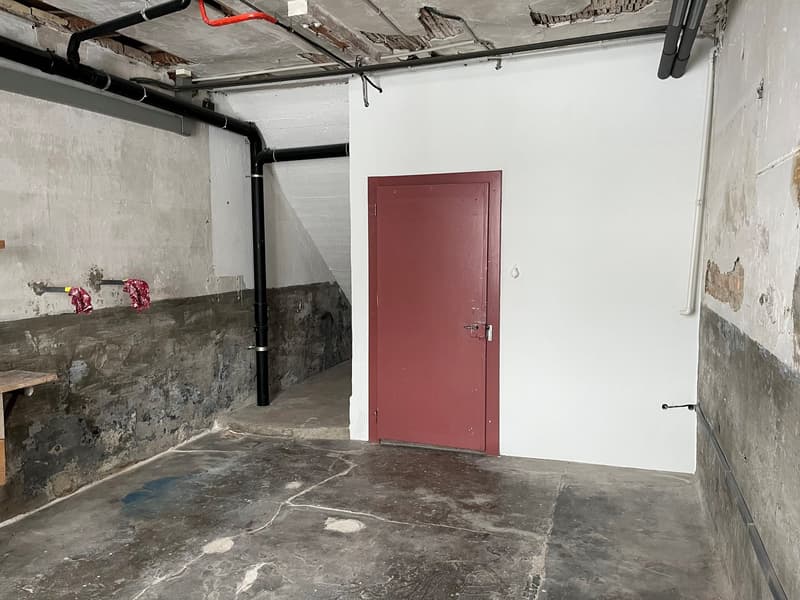 empty room, red door, concrete floor, black pipe on ceiling, small wooden desk