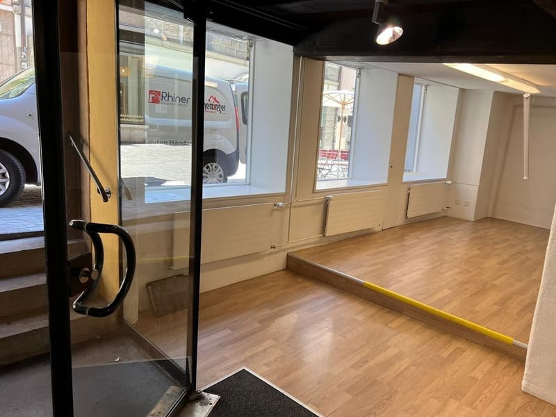 entrance hall with wooden floor, glass doors, a mat at the entrance, an office in the corner, and a white van reflected in the window