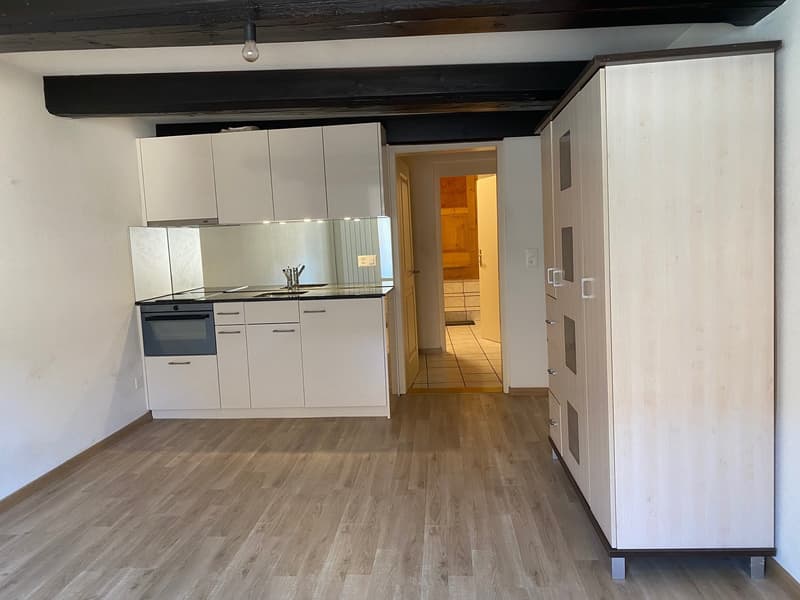 an empty kitchen with wooden floor, white cabinets, an oven, a sink, and a faucet