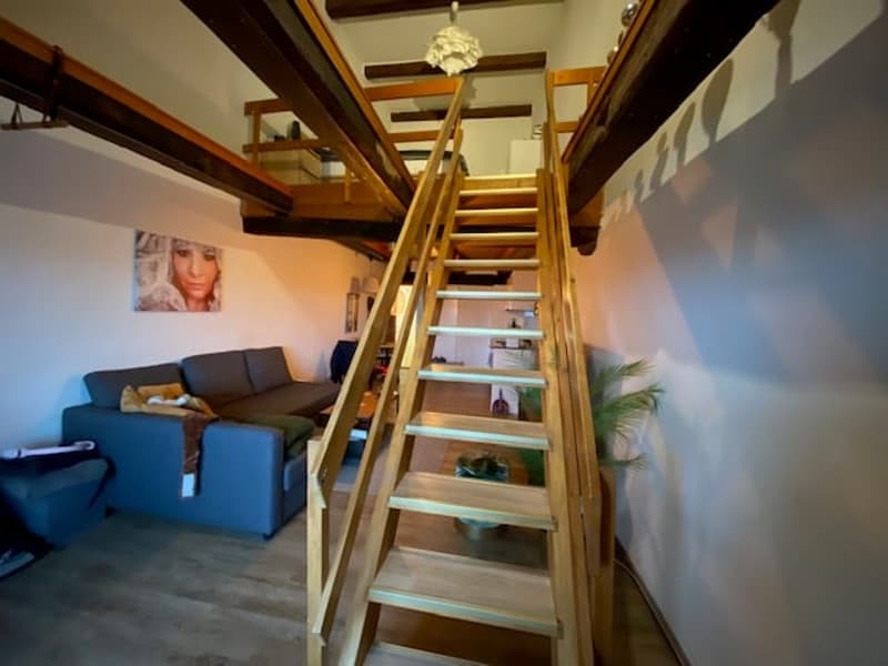Living area with wooden stairs, grey couch, and wooden floors
