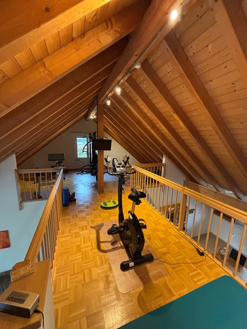 A gym in the attic with wooden beams, a wooden floor, and various exercise equipment.