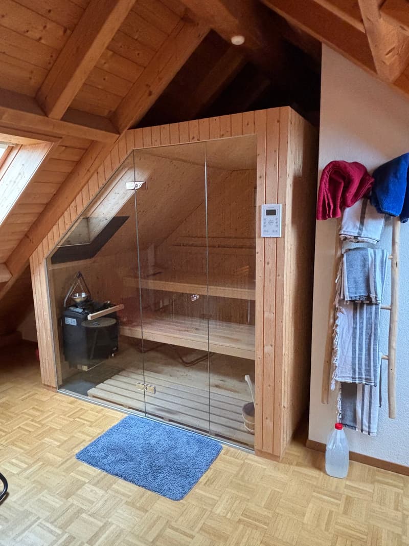 wooden sauna, glass door, wooden benches, control panel, blue rug, towels