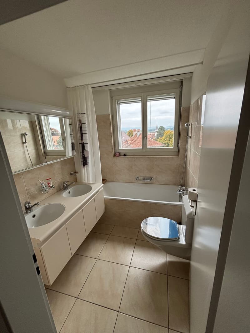 Bathroom with two sinks, bathtub, toilet, mirror, and window