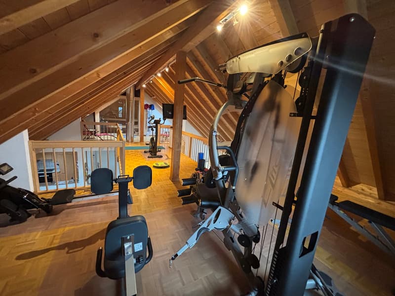 A gym in the attic with various exercise equipment, wooden floor, wooden beams, and a window.