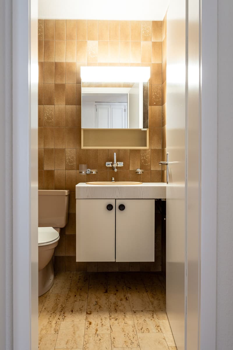 Bathroom with beige tiles, white sink, mirror, toilet, wooden floor