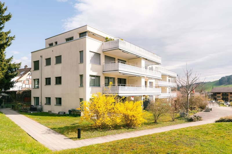 Modern white building, multiple balconies, well-maintained garden, paved walkway