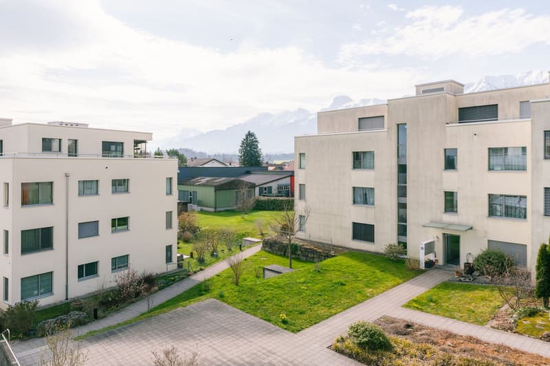 Two white apartment buildings, paved walkway, green lawn, mountain view