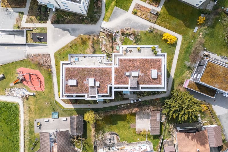 Modern house with green roof, multiple balconies, surrounded by grass and trees