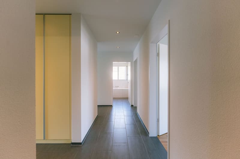 Empty hallway with white walls, tiled floor, and a yellow wardrobe on the left side.