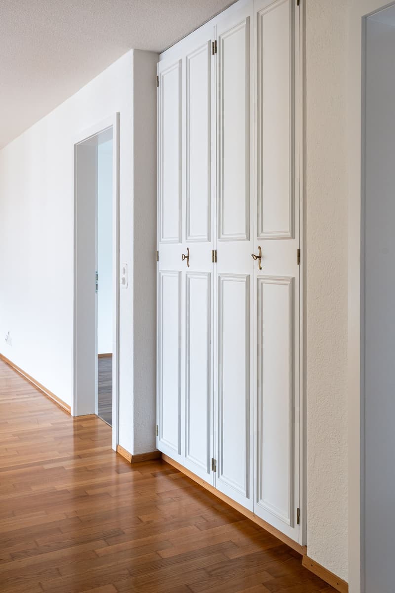 Empty room with white walls, wooden floor, and large white closets
