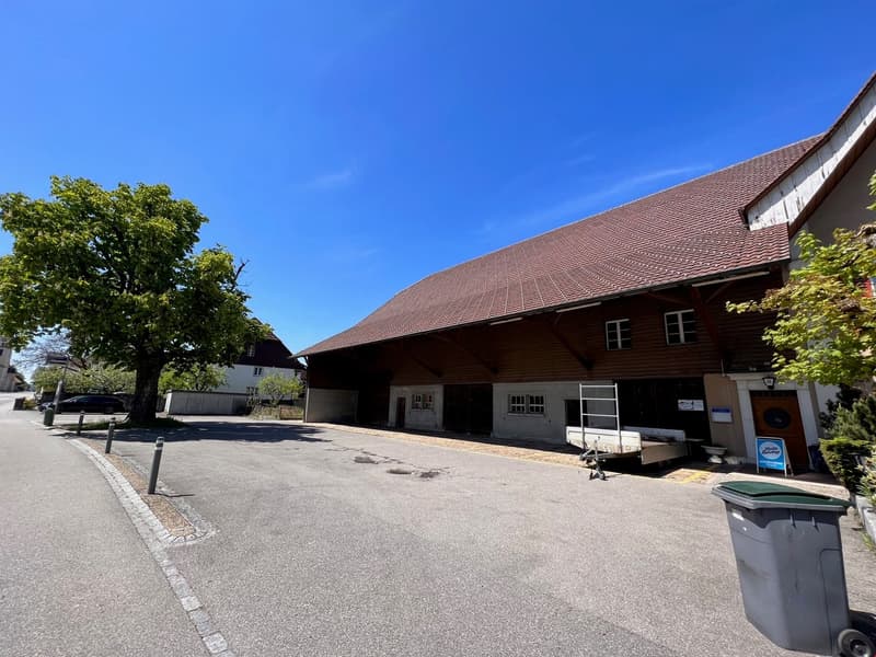 large building with brown roof, garage, parking in front, trees, street