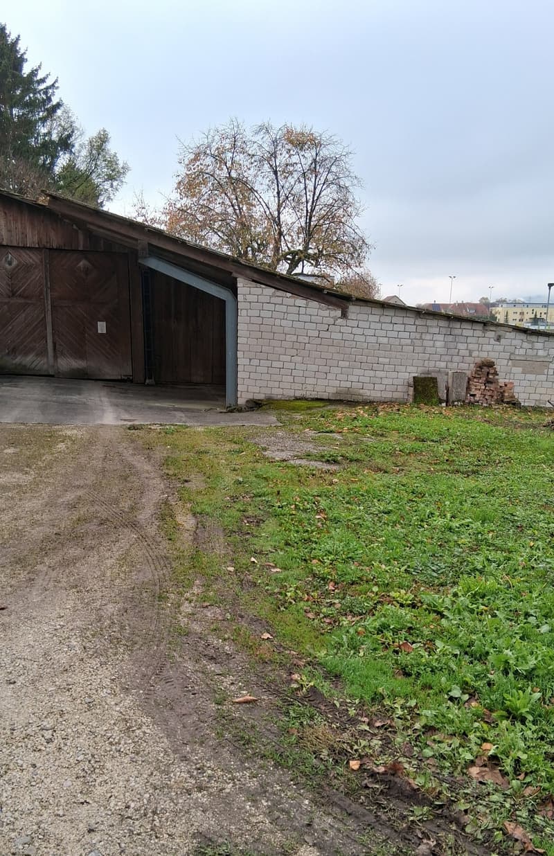 Garage attached to a brick wall, dirt path, grass area, trees